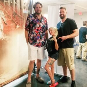 Daisy Chain standing between two tall men to show her 4'11" height at a public event.